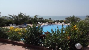 A pool area with lounge chairs and palm trees, overlooking the sea. - Maya (Cap Skirring)