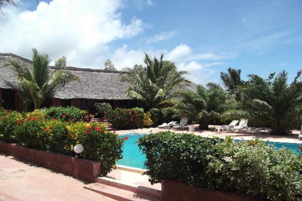 A pool area with lounge chairs, a thatched-roof building, and lush greenery.