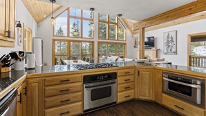 Una cocina moderna con armarios de madera, una isla central, electrodomésticos de acero inoxidable y grandes ventanas con vistas al exterior.