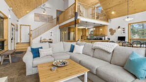 Amplia sala de estar con un sofá modular grande, una mesa de centro de madera y una escalera que lleva a un nivel superior.