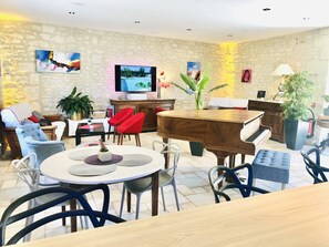 A living room with a piano, red chairs, a television, and a stone wall. - Hotel the Originals Pigeonnier Du Perron (Availles-en-Chatellerault)