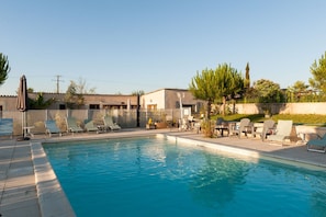 A swimming pool with lounge chairs and a table, surrounded by a fence and vegetation. - Hotel the Originals Pigeonnier Du Perron (Availles-en-Chatellerault)
