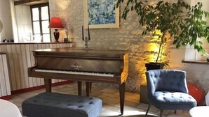 A piano, a blue armchair, and a dining table in a room with stone walls and a tiled floor. - Hotel the Originals Pigeonnier Du Perron (Availles-en-Chatellerault)