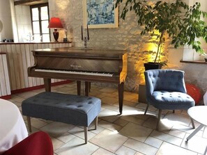 Um piano, uma poltrona azul e uma mesa de jantar em um quarto com paredes de pedra e piso ladrilhado.