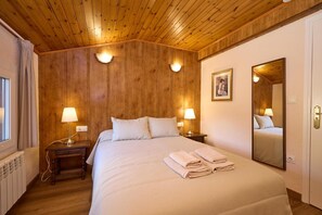 A hotel room with a wooden ceiling, a large bed with white linens, two bedside tables with lamps, a large mirror, and a window with curtains. - Peretol (Bordes d'Envalira)
