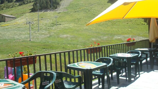 A terrace with outdoor seating, a yellow umbrella, and a view of a green hillside. - Peretol (Bordes d'Envalira)
