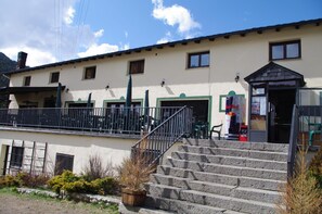 A building with a staircase leading to a door, a Red Bull vending machine, and a small outdoor seating area. - Peretol (Bordes d'Envalira)