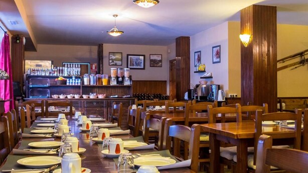A restaurant with wooden tables and chairs, a bar area in the background, and hanging pendant lights. - Peretol (Bordes d'Envalira)