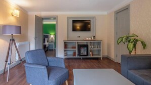 A modern living room with a grey sofa, a coffee table, a floor lamp, a flat-screen TV mounted on the wall, and a bookshelf with various items. - Sairme Hotels & Resorts (Sairme)
