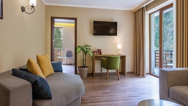 A modern hotel room with a sofa, a desk, a TV, and a balcony with curtains. - Sairme Hotels & Resorts (Sairme)