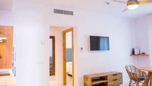 A modern living room with a flat-screen TV, wooden furniture, and a ceiling fan. - Sa Cala Suites (Formentera)