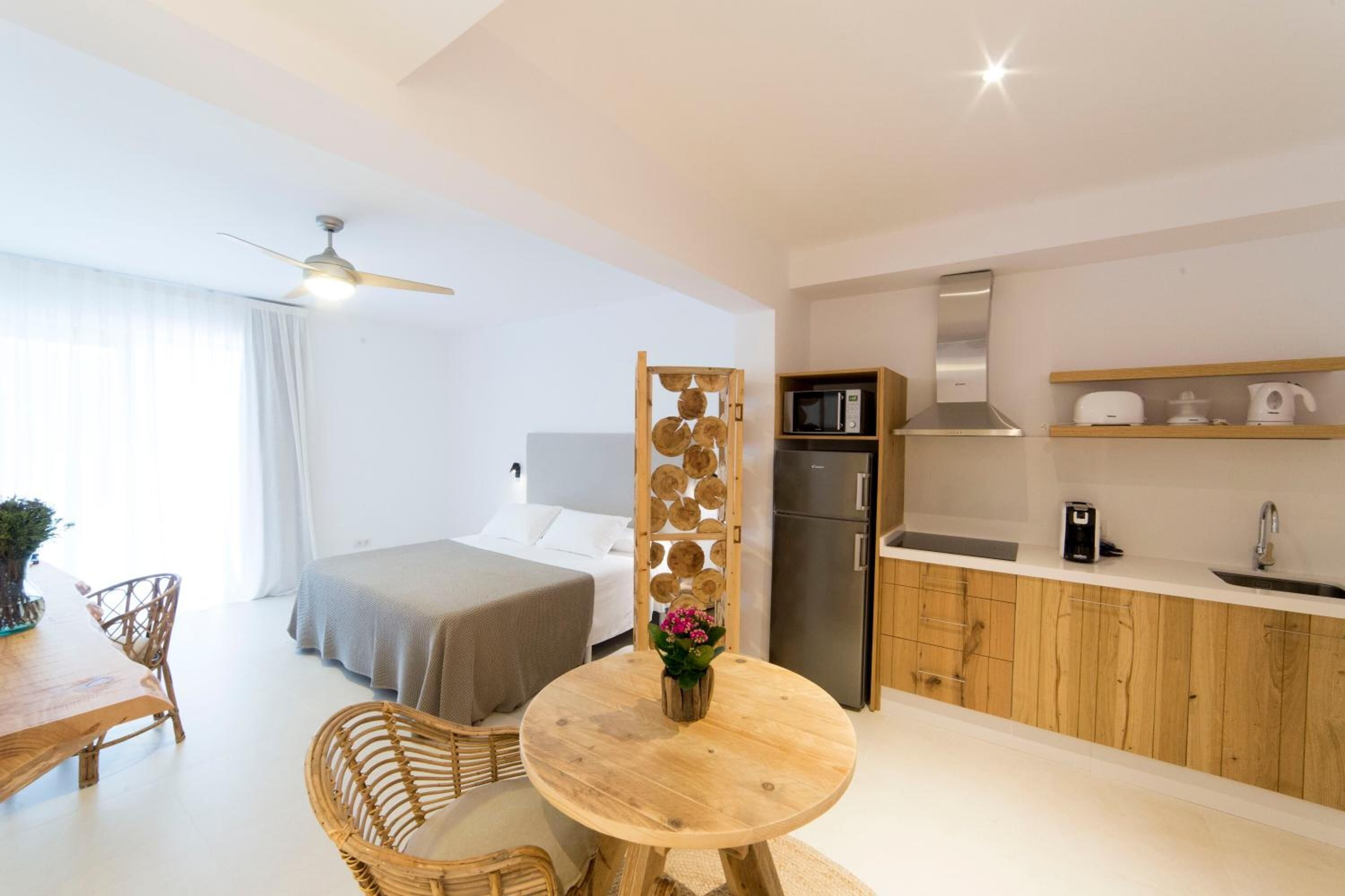 Una camera d'albergo compatta con un letto, un tavolo da pranzo con sedie, un angolo cottura e una ventola a soffitto.