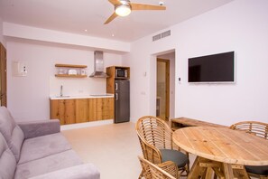 A modern kitchen with wooden cabinets, a built-in microwave, and a stainless steel refrigerator. There is a dining area with a wooden table and wicker chairs. - Sa Cala Suites (Formentera)