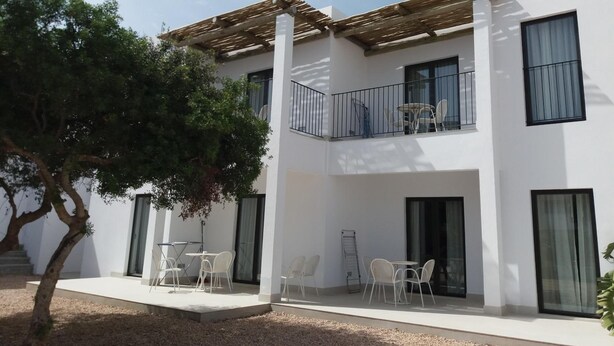 A modern two-story building with a covered patio area, outdoor seating, and a tree. - Sa Cala Suites (Formentera)