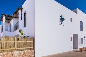 A modern building with a white facade, a wooden fence, and a stone wall. - Sa Cala Suites (Formentera)
