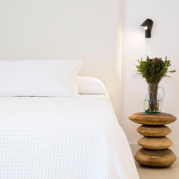 A neatly made bed with a white pillow and a textured white bedspread. - Sa Cala Suites (Formentera)