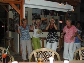Un grupo de personas bailando en un restaurante con muebles de madera y una zona de bar al fondo.