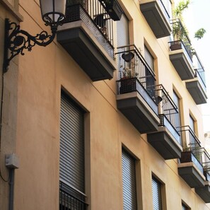 A building with multiple balconies, a closed shuttered window, and a decorative light fixture. - Apartamentos El Carmen by Be Alicante (Alicante)