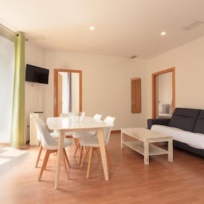 A modern living room with a dining table, chairs, a sofa, and a television mounted on the wall. - Apartamentos El Carmen by Be Alicante (Alicante)