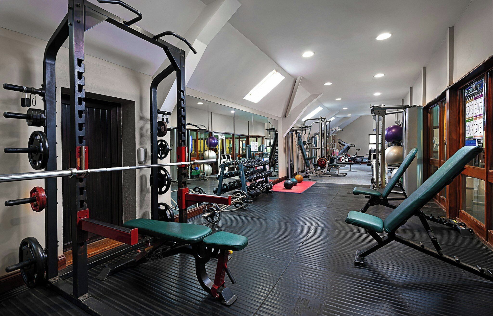 Un gimnasio con equipo de levantamiento de pesas, bancos y un espejo grande.