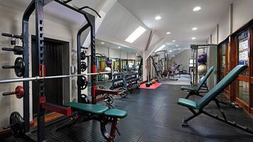 Un gimnasio con equipo de levantamiento de pesas, bancos y un espejo grande.