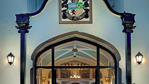 Una entrada de hotel con un escudo de armas, una imponente escalera y un candelabro.
