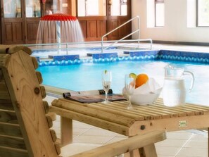 Uma cadeira de lounge de madeira ao lado de uma piscina, com um jarro de vidro, uma tigela de frutas e um copo de água.