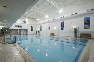 Una piscina interior con carriles delimitados, suelo de baldosas y techo con vigas a la vista.