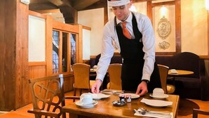 A person setting a table in a restaurant with wooden interiors and a chandelier. - Carrigaline Court Hotel And Leisure Centre (Carrigaline)