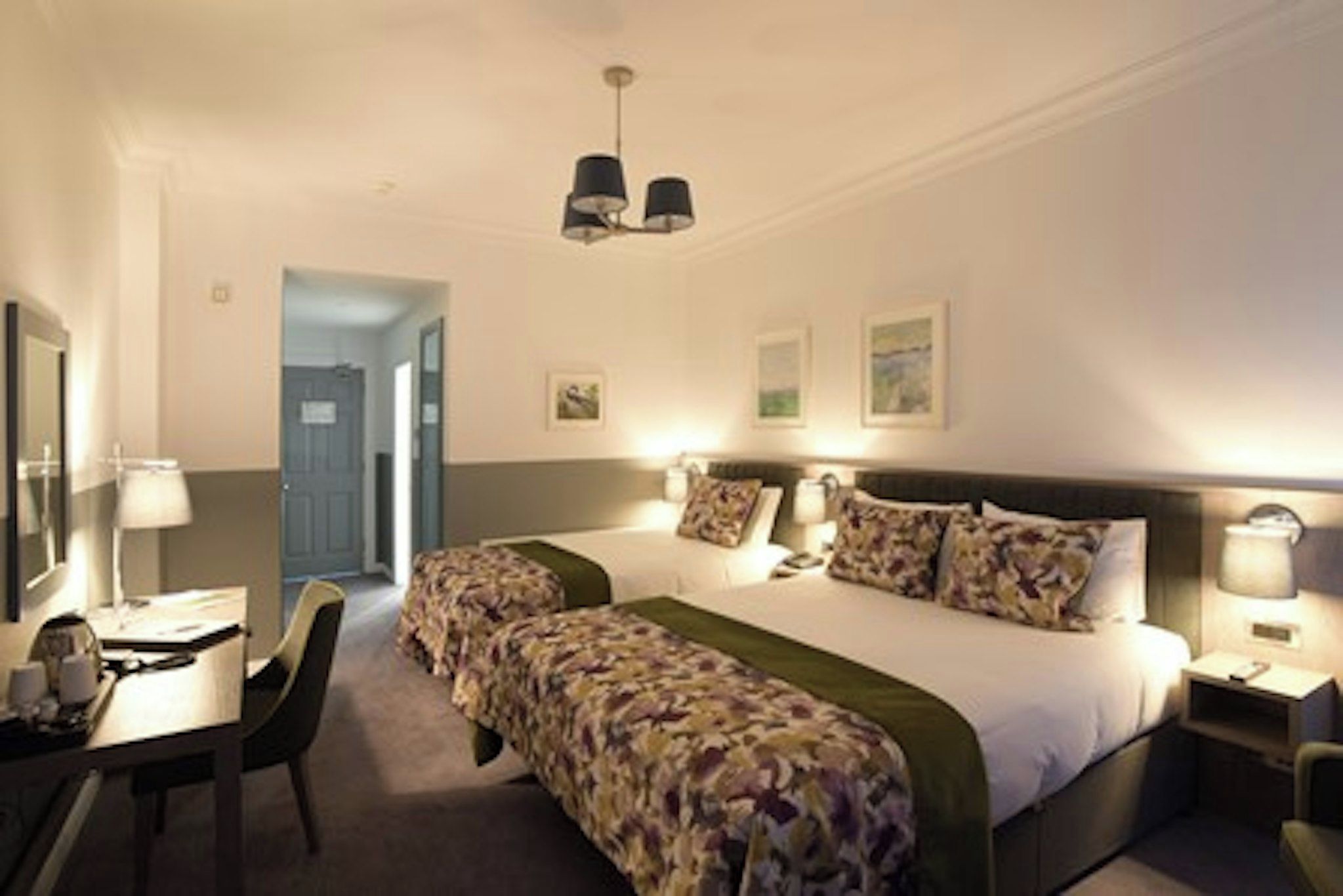 A hotel room with two beds, a desk, a chair, and a door leading to another room.