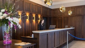 A reception desk with a wooden panel backdrop, a vase of flowers, and a blue rope barrier. - Carrigaline Court Hotel And Leisure Centre (Carrigaline)