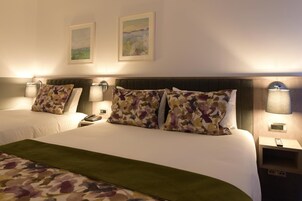 Habitación de hotel con dos camas, cada una con una mesita de noche, una lámpara y un teléfono. Dos cuadros enmarcados adornan la pared sobre las camas.