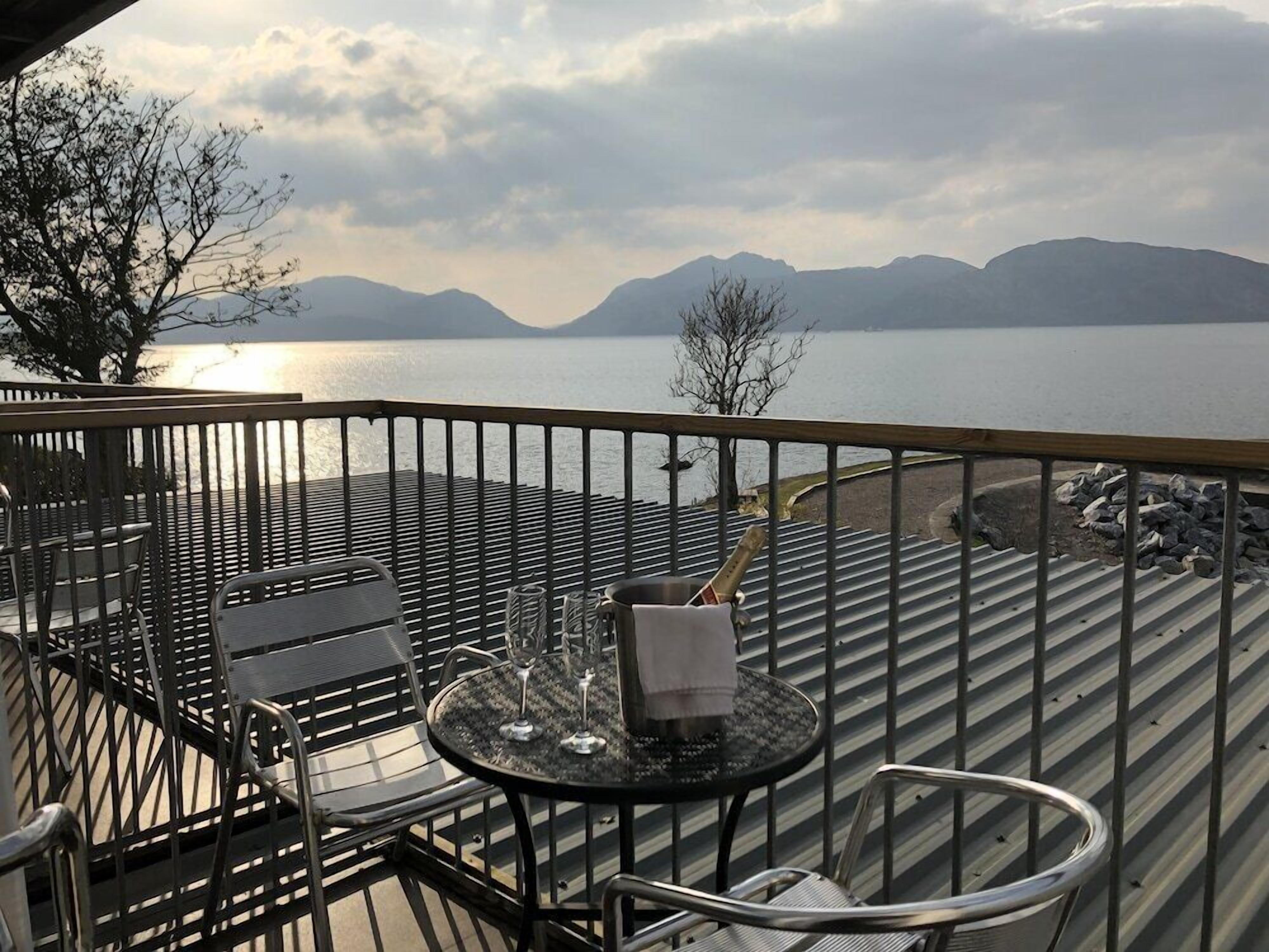 A balcony with a table and chairs overlooking a body of water and mountains.