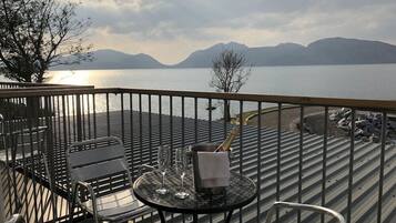 A balcony with a table and chairs overlooking a body of water and mountains.