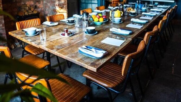 A long wooden table set for a meeting with chairs, a projector screen, and various items on the table. - The Vicarage (Crewe)