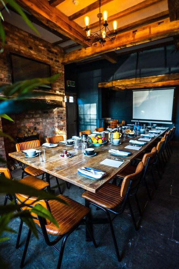 A long wooden table set for a meeting with chairs, a projector screen, and various items on the table. - The Vicarage (Crewe)