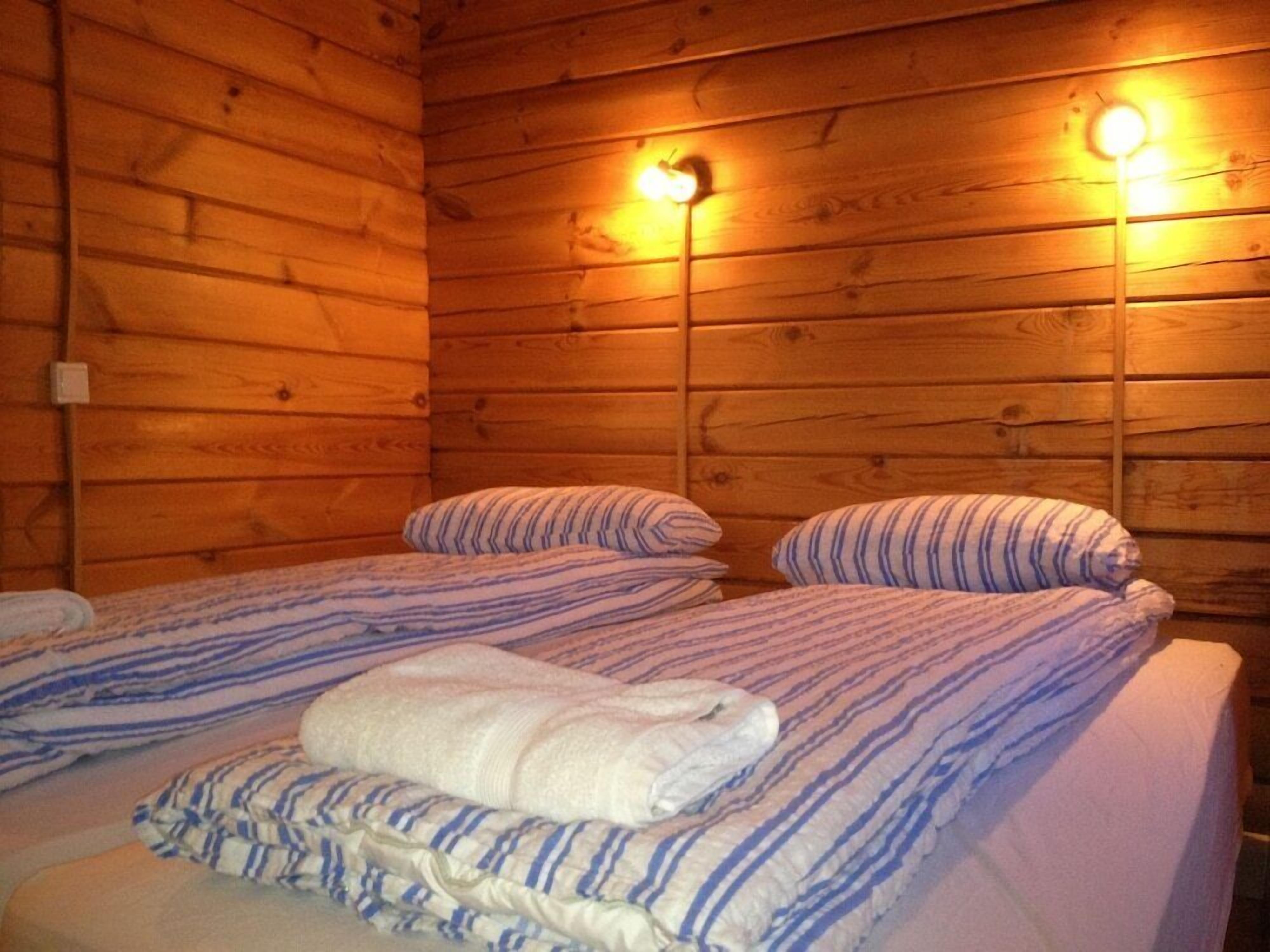 Habitación de cabaña de madera con dos camas, cada una con ropa de cama a rayas y almohadas, y dos luces fijadas a la pared.