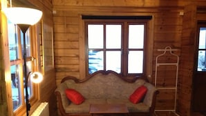 A cozy room with a wooden interior, a sofa with red cushions, a small table, and a radiator. - North Star Guesthouse (Rangárþing eystra)