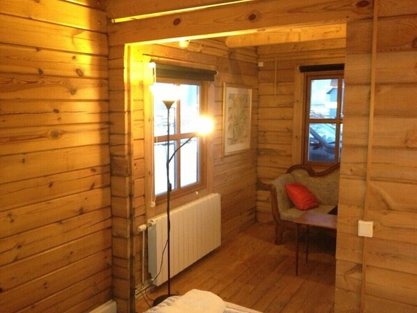 A cozy cabin room with wooden walls, a radiator, a window, a chair, and a table. - North Star Guesthouse (Rangárþing eystra)