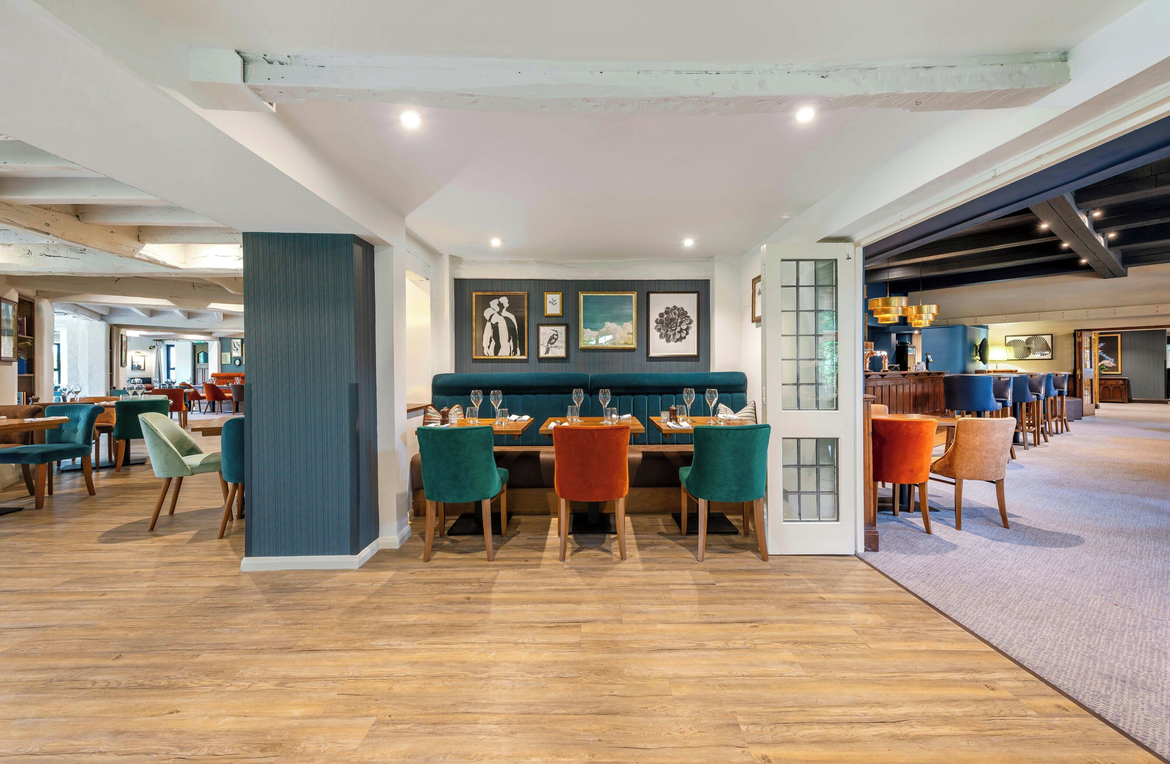 Un restaurante amplio con suelos de madera, sillas color aguamarina y naranja, y una variedad de obras de arte enmarcadas en las paredes.