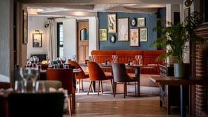 Un restaurante con techo de madera, pared azul con obras de arte enmarcadas, un banco rojo y una zona de comedor con mesas y sillas.