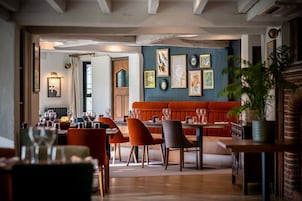 Restaurante com teto de madeira, parede azul com obras de arte emolduradas, um banco vermelho e área de refeições com mesas e cadeiras.