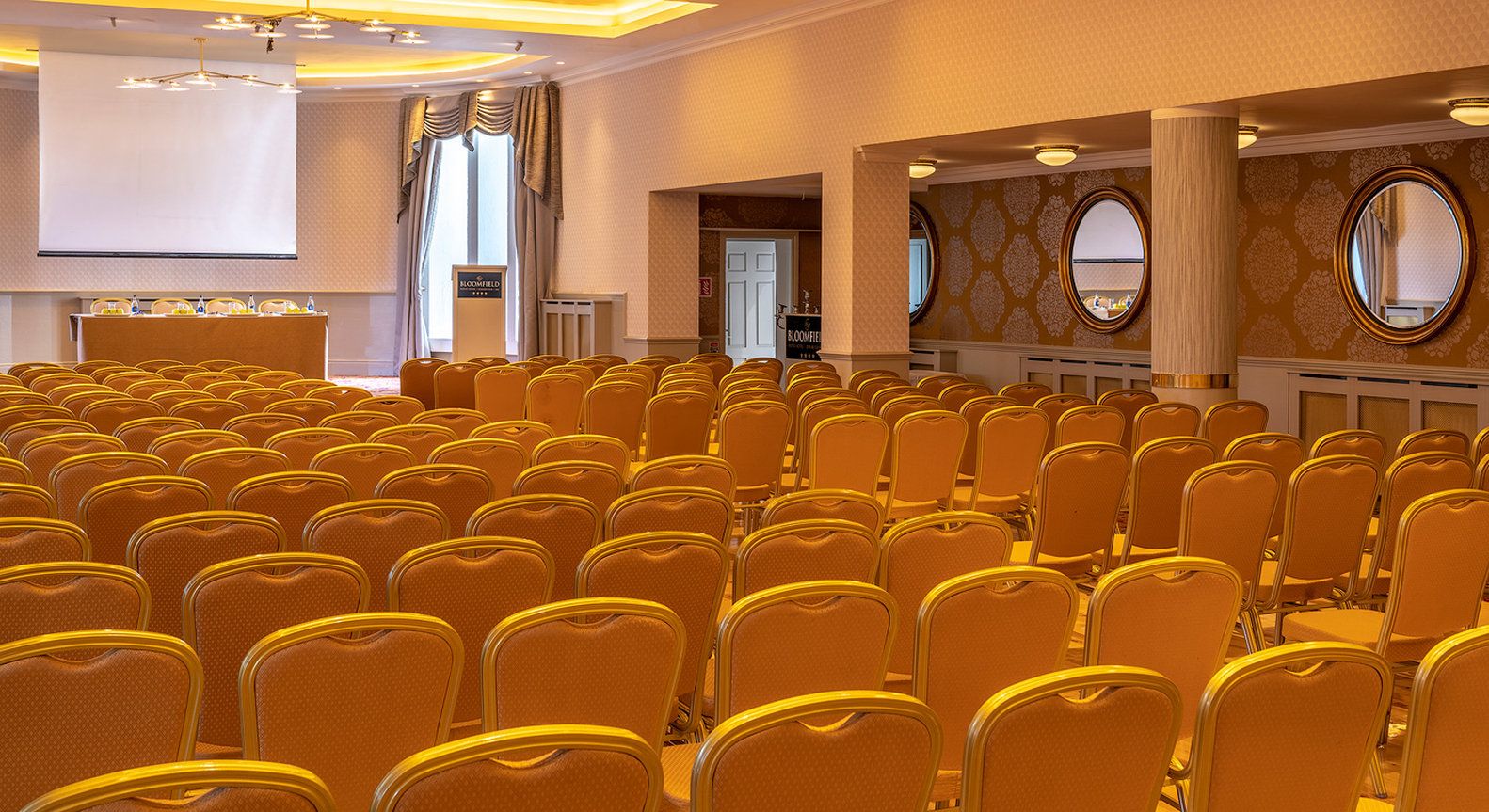 A conference room with rows of chairs, a podium, and a projection screen.