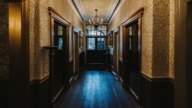 A long, narrow hallway with patterned wallpaper, wooden doors, and a chandelier. - Brook Hall Hotel (Ellesmere Port)
