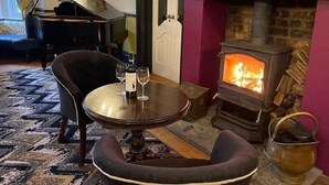 A cozy room with a fireplace, a piano, and a table with wine glasses. - Brook Hall Hotel (Ellesmere Port)
