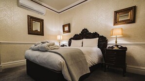 A neatly made bed with a blanket, a bedside lamp, and a small wooden nightstand. - Brook Hall Hotel (Ellesmere Port)