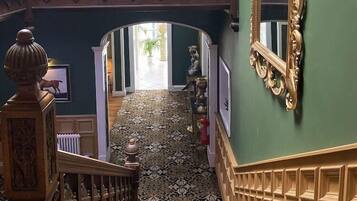 Un interior imponente con una escalera de madera, barandales ornamentados y un espejo grande.