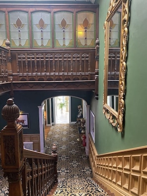 A grand interior with a wooden staircase, ornate balustrades, and a large mirror. - Stone House (Stone)