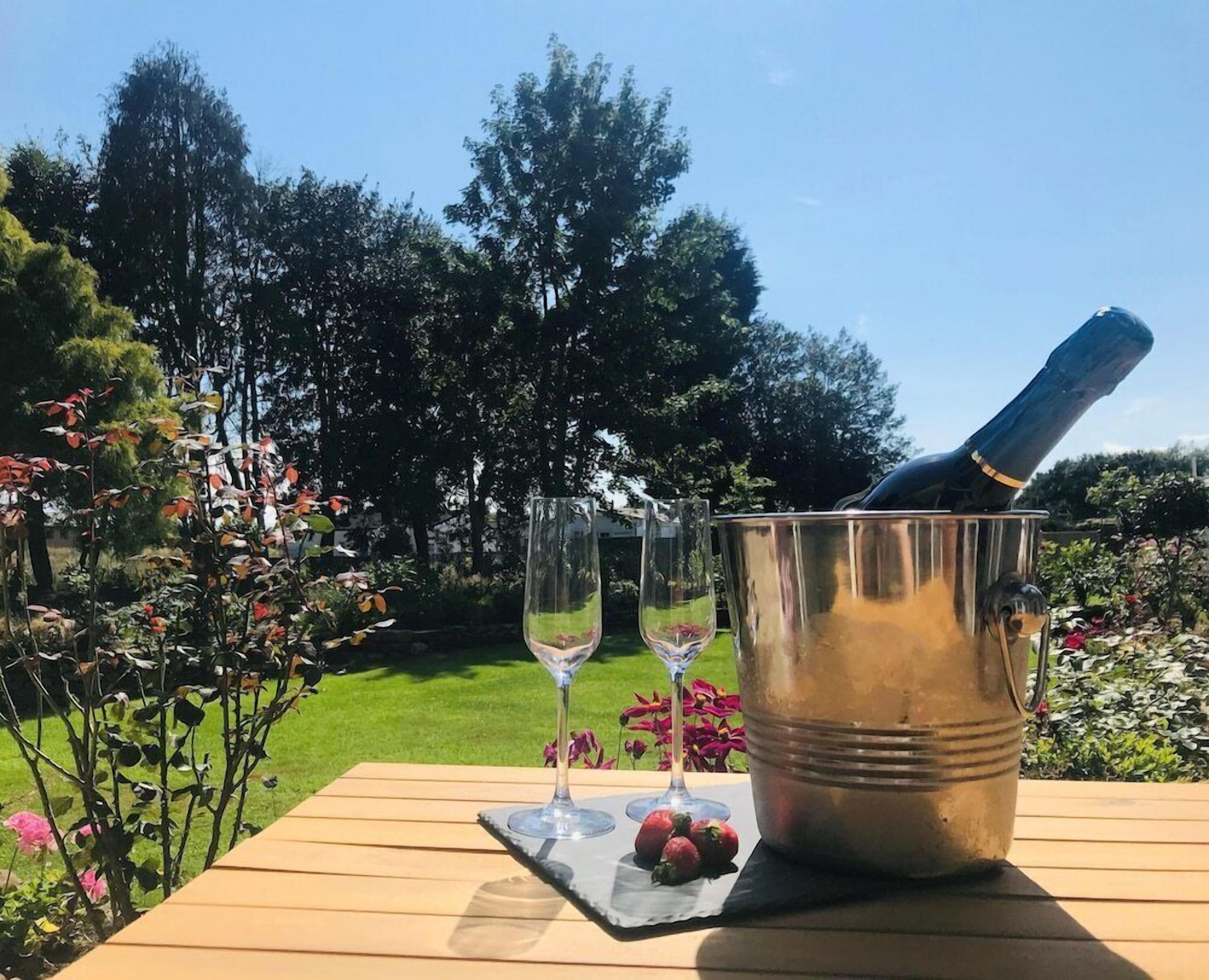 Una mesa de madera con un balde de metal que contiene una botella y dos copas de vino vacías.
