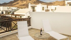 A rooftop terrace with two white lounge chairs, a small round table, and a bottle of wine. The terrace overlooks a mountainous landscape and white buildings. - Playa Blanca Beach Mate (Yaiza)